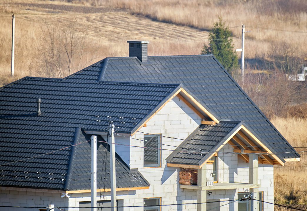 A new house under construction with a modern, dark-colored tile roof.