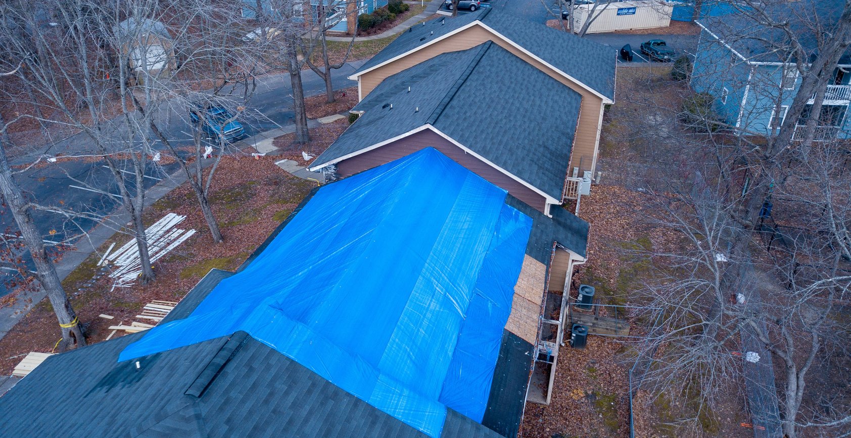 A residential building with a damaged roof covered by a large blue tarp.